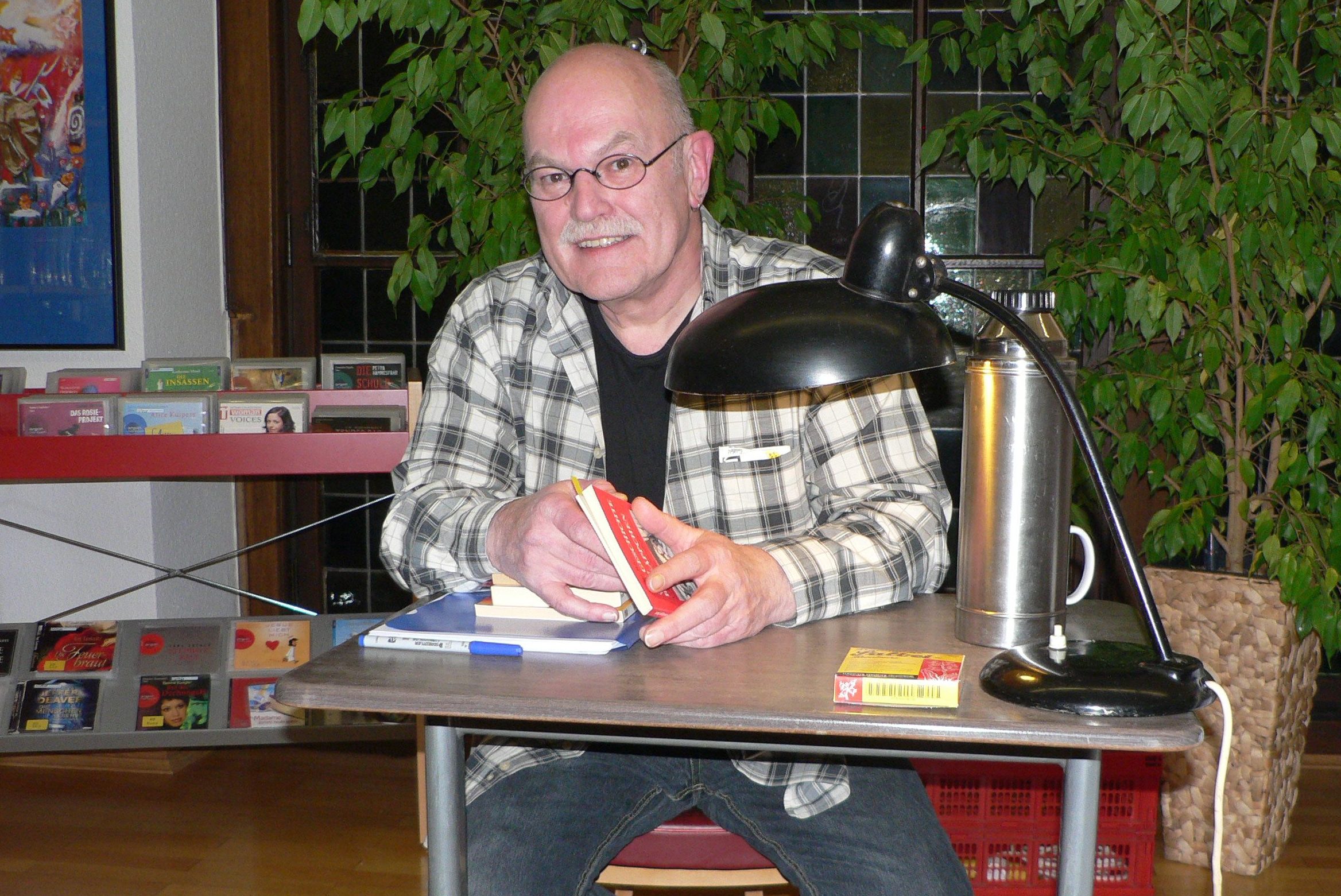 Thomas J. Lennartz, wie wir ihn kennen: schwarze Jeans, kariertes Hemd, alte Schreibtischlampe und Thermoskanne